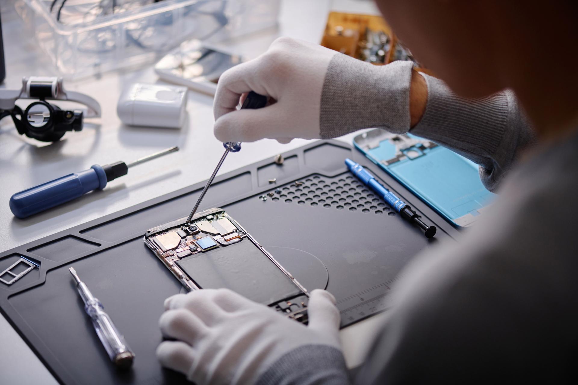 Professional Repairman Working on Broken Cellphone at His Desk in Workshop