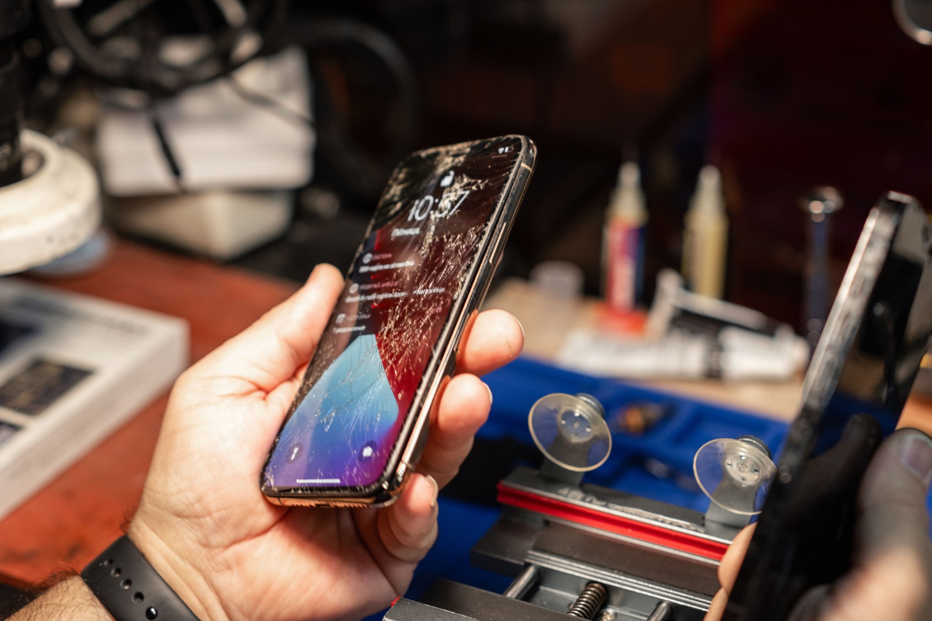 A technician examines a smartphone with shattered glass in a phone repair shop during a busy afternoon