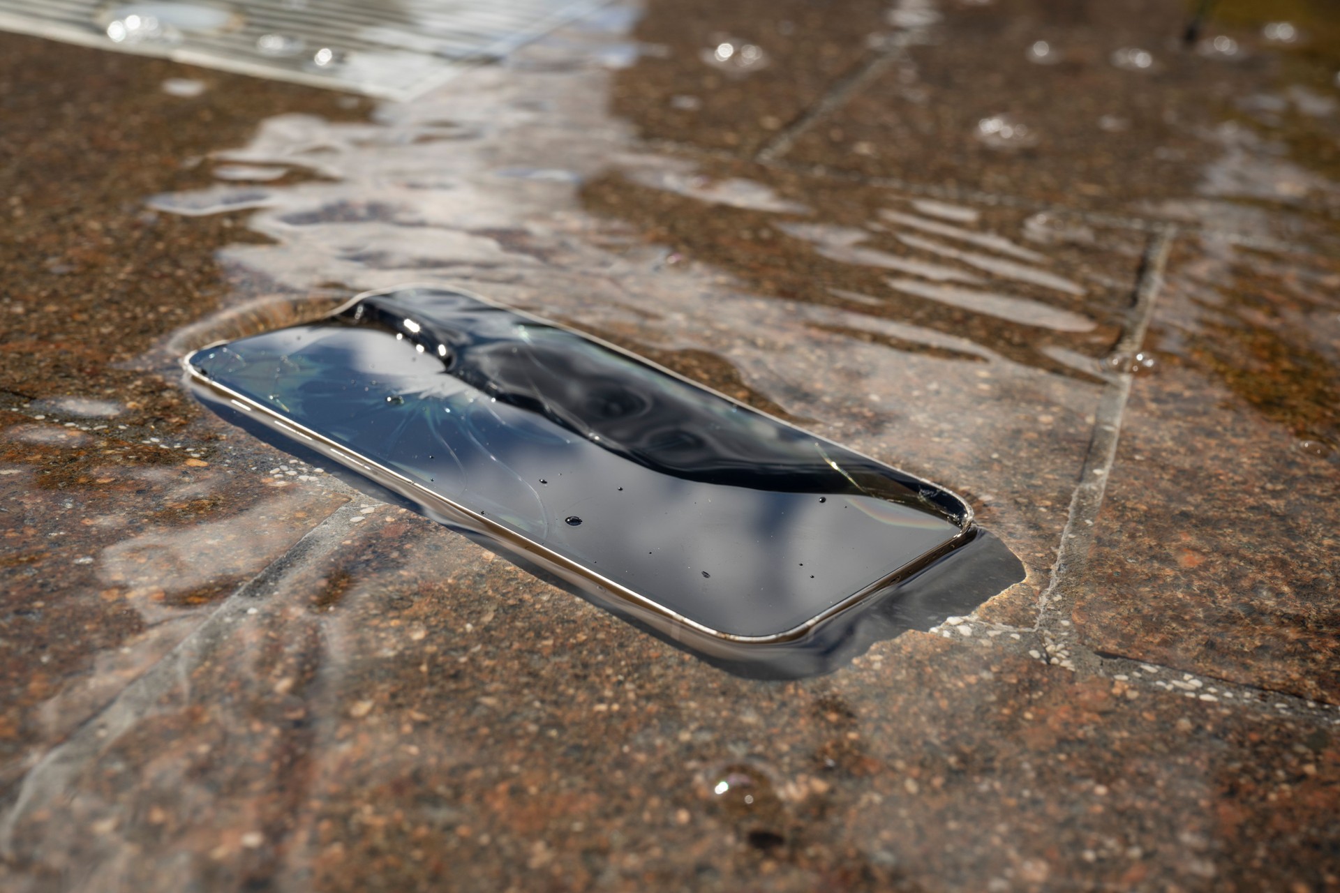 Broken smartphone submerged in water on stone surface